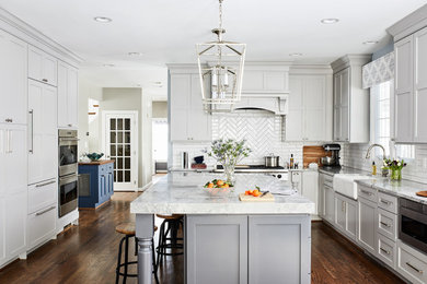 Design ideas for a large traditional u-shaped kitchen in Chicago with a farmhouse sink, shaker cabinets, grey cabinets, quartzite benchtops, porcelain splashback, stainless steel appliances, with island, brown floor, grey benchtop, white splashback and dark hardwood floors.