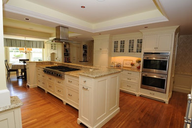 Inspiration for a large traditional galley open plan kitchen in Manchester with beaded inset cabinets, an undermount sink, white cabinets, granite benchtops, stainless steel appliances, dark hardwood floors, with island, brown floor, beige benchtop, white splashback and subway tile splashback.
