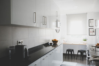 Modelo de cocina lineal contemporánea de tamaño medio cerrada sin isla con fregadero bajoencimera, armarios con paneles lisos, puertas de armario blancas, encimera de cuarzo compacto, salpicadero blanco, salpicadero de azulejos de cerámica, electrodomésticos de acero inoxidable, suelo de baldosas de porcelana, suelo gris y encimeras negras
