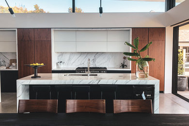 Large galley open plan kitchen in Sydney with a drop-in sink, flat-panel cabinets, dark wood cabinets, marble benchtops, white splashback, marble splashback, stainless steel appliances, concrete floors, with island, grey floor and white benchtop.