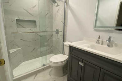 Bathroom - mid-sized transitional white tile and marble tile marble floor, white floor and single-sink bathroom idea in Miami with recessed-panel cabinets, gray cabinets, a two-piece toilet, gray walls, an integrated sink, quartz countertops, white countertops and a freestanding vanity