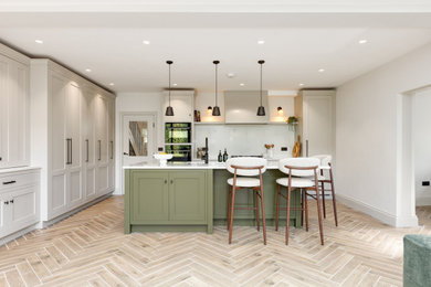 Inspiration for an expansive classic l-shaped open plan kitchen in Hertfordshire with shaker cabinets, beige cabinets, engineered stone countertops, white splashback, engineered quartz splashback, black appliances, an island, beige floors and white worktops.