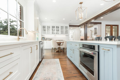 Large classic open plan kitchen in New Orleans with a submerged sink, flat-panel cabinets, white cabinets, engineered stone countertops, white splashback, metro tiled splashback, stainless steel appliances, dark hardwood flooring, brown floors and white worktops.