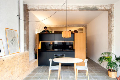 Photo of a small industrial single-wall open plan kitchen in Barcelona with a single-bowl sink, flat-panel cabinets, black cabinets, quartz benchtops, black splashback, panelled appliances, concrete floors, no island and grey floor.