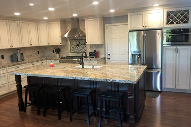 Example of a mid-sized classic l-shaped dark wood floor and brown floor eat-in kitchen design in San Francisco with an undermount sink, flat-panel cabinets, white cabinets, granite countertops, beige backsplash, travertine backsplash, stainless steel appliances, an island and multicolored countertops