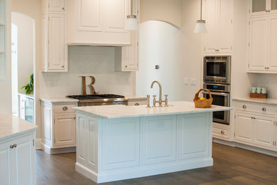 Mid-sized tuscan u-shaped medium tone wood floor eat-in kitchen photo in Jacksonville with a farmhouse sink, shaker cabinets, white cabinets, quartz countertops, white backsplash, ceramic backsplash, stainless steel appliances and an island