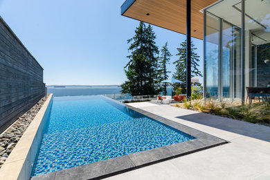 Medium sized modern back rectangular infinity swimming pool in Vancouver with tiled flooring.
