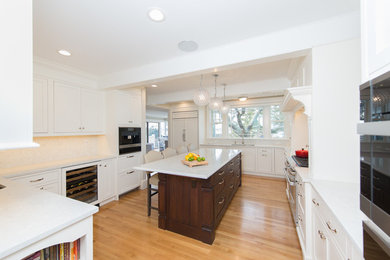 Large beach style kitchen in Providence with an undermount sink, shaker cabinets, white cabinets, quartz benchtops, white splashback, panelled appliances, medium hardwood floors, with island and white benchtop.