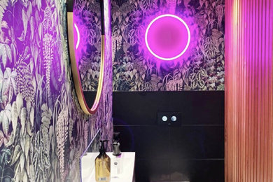Design ideas for an eclectic powder room in Christchurch with raised-panel cabinets, black cabinets, a one-piece toilet, black tile, ceramic tile, ceramic floors, a drop-in sink, laminate benchtops, black floor, a floating vanity, wood and wallpaper.