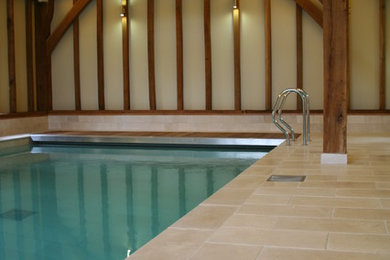 This is an example of a large traditional indoor rectangular pool in Berkshire with a pool house and natural stone pavers.