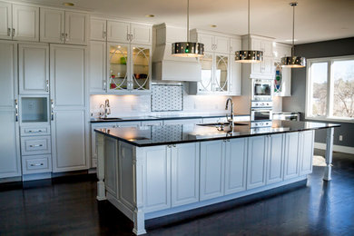 Inspiration for a large timeless galley dark wood floor and brown floor open concept kitchen remodel in Denver with an undermount sink, raised-panel cabinets, white cabinets, solid surface countertops, white backsplash, stainless steel appliances and an island