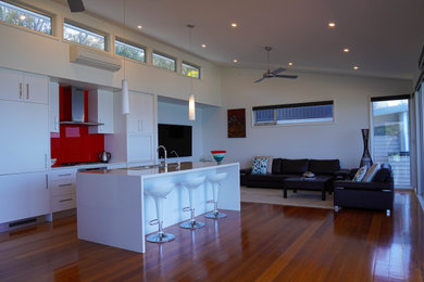 Design ideas for a mid-sized modern galley open plan kitchen in Geelong with a double-bowl sink, flat-panel cabinets, white cabinets, quartz benchtops, red splashback, white appliances, medium hardwood floors, with island and white benchtop.