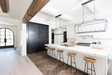 Example of a large tuscan medium tone wood floor open concept kitchen design in Phoenix with an island, white cabinets, white backsplash, white countertops, shaker cabinets and paneled appliances