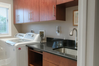 This is an example of a mid-sized contemporary single-wall dedicated laundry room in Other with an undermount sink, flat-panel cabinets, medium wood cabinets, beige walls, a side-by-side washer and dryer and beige floor.