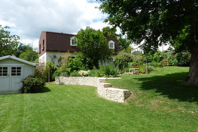 Réalisation d'un grand jardin à la française style shabby chic au printemps avec un massif de fleurs, une exposition ensoleillée, une pente, une colline ou un talus, des pavés en pierre naturelle et une clôture en bois.
