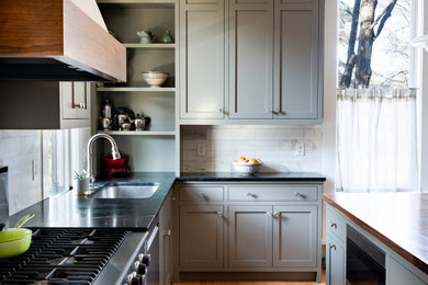 Mid-sized elegant light wood floor eat-in kitchen photo in Minneapolis with an undermount sink, shaker cabinets, gray cabinets, soapstone countertops, white backsplash, marble backsplash, an island and black countertops