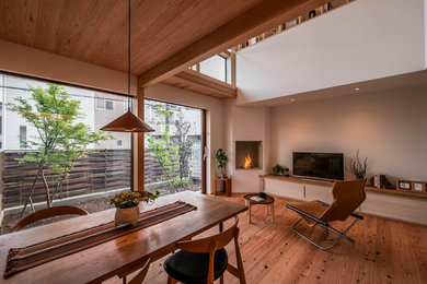 Cette image montre une salle à manger ouverte sur la cuisine avec un mur blanc, un sol en bois brun, une cheminée d'angle, un manteau de cheminée en pierre et poutres apparentes.