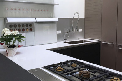Inspiration for a small modern u-shaped kitchen in Other with a submerged sink, flat-panel cabinets, brown cabinets, glass worktops, white splashback, glass tiled splashback, stainless steel appliances, medium hardwood flooring and white worktops.