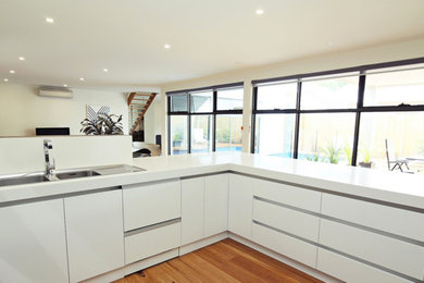 Inspiration for a mid-sized contemporary u-shaped open plan kitchen in Melbourne with a double-bowl sink, flat-panel cabinets, white cabinets, granite benchtops, stainless steel appliances, medium hardwood floors and no island.