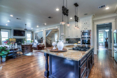 Open concept kitchen - large traditional l-shaped dark wood floor and brown floor open concept kitchen idea in Houston with a farmhouse sink, beaded inset cabinets, white cabinets, granite countertops, gray backsplash, ceramic backsplash, stainless steel appliances and an island