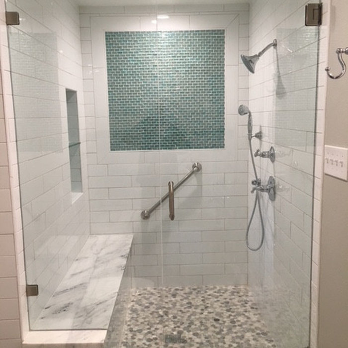 This accessible, modern walk-in shower features key aging-in-place renovation upgrades, including a curbless entry, built-in marble bench, secure stainless steel grab bar, and a handheld showerhead. W