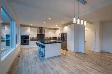 Eat-in kitchen - large modern l-shaped vinyl floor and gray floor eat-in kitchen idea in Other with white cabinets, granite countertops, gray backsplash, glass tile backsplash, black appliances, an island and black countertops