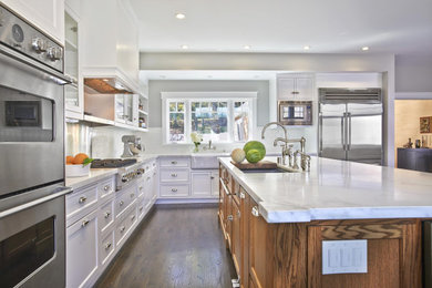 Example of a trendy coffered ceiling kitchen design in San Francisco with glass-front cabinets, medium tone wood cabinets, metallic backsplash, stainless steel appliances and white countertops
