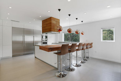 Mid-sized trendy u-shaped concrete floor eat-in kitchen photo in Miami with an undermount sink, flat-panel cabinets, white cabinets, wood countertops, stainless steel appliances and a peninsula