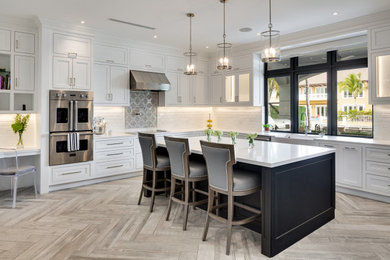 Expansive transitional l-shaped eat-in kitchen in Miami with a farmhouse sink, shaker cabinets, white cabinets, quartz benchtops, white splashback, subway tile splashback, stainless steel appliances, porcelain floors, with island, grey floor and white benchtop.