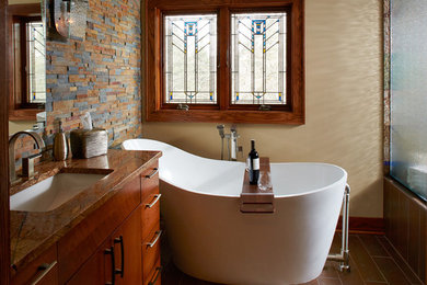 Photo of a country master bathroom in Minneapolis with an undermount sink, flat-panel cabinets, medium wood cabinets, granite benchtops, a freestanding tub, an alcove shower, brown tile, stone tile, multi-coloured walls and ceramic floors.