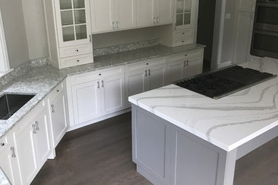 Example of a large trendy l-shaped dark wood floor and brown floor enclosed kitchen design in New York with an undermount sink, shaker cabinets, white cabinets, quartz countertops, stainless steel appliances and an island