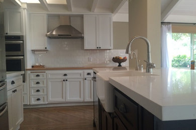 Inspiration for a large contemporary u-shaped medium tone wood floor eat-in kitchen remodel in San Francisco with a farmhouse sink, shaker cabinets, white cabinets, quartzite countertops, white backsplash, subway tile backsplash, stainless steel appliances and an island