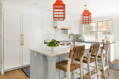 Beach style l-shaped medium tone wood floor kitchen photo in Minneapolis with a farmhouse sink, shaker cabinets, white cabinets, gray backsplash, stainless steel appliances, an island and black countertops