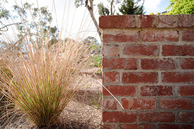 This is an example of a front yard full sun xeriscape for spring in Melbourne with a retaining wall and brick pavers.