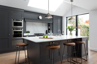 This is an example of a large modern single-wall eat-in kitchen in Dublin with a single-bowl sink, shaker cabinets, grey cabinets, quartzite benchtops, white splashback, stone slab splashback, stainless steel appliances, medium hardwood floors, with island, brown floor and white benchtop.