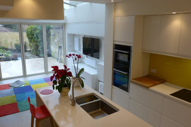 Mid-sized contemporary l-shaped open plan kitchen in Other with a drop-in sink, flat-panel cabinets, white cabinets, quartzite benchtops, yellow splashback, glass sheet splashback, stainless steel appliances, porcelain floors, with island, beige floor, white benchtop and vaulted.