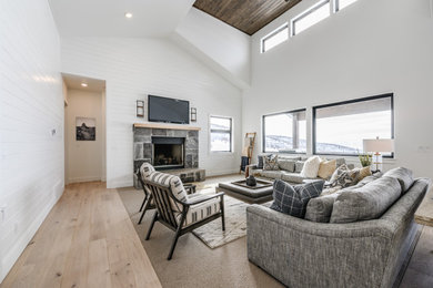 Example of a country open concept medium tone wood floor and brown floor living room design in Salt Lake City with white walls, a standard fireplace, a stone fireplace and a wall-mounted tv