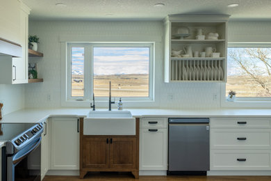 他の地域にあるカントリー風のおしゃれなキッチン (フラットパネル扉のキャビネット、白いキャビネット、シルバーの調理設備、茶色い床、白いキッチンカウンター、白いキッチンパネル) の写真