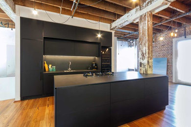 Small industrial galley eat-in kitchen in Sydney with an undermount sink, black cabinets, black splashback, panelled appliances, medium hardwood floors, with island, brown floor and black benchtop.
