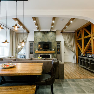 Modelo de salón abierto, mediterráneo, grande, con chimenea lineal, marco de chimenea de piedra, televisor colgado en la pared y suelo laminado