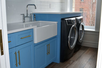 Inspiration for a mid-sized transitional ceramic tile and brown floor laundry room remodel in New York with a farmhouse sink, shaker cabinets, blue cabinets, quartz countertops, white walls, a side-by-side washer/dryer and white countertops