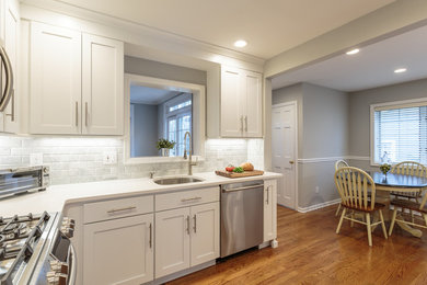 Small minimalist l-shaped medium tone wood floor enclosed kitchen photo in New York with an undermount sink, shaker cabinets, white cabinets, quartz countertops, white backsplash, stone tile backsplash, stainless steel appliances and no island