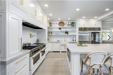 Design ideas for an expansive transitional l-shaped separate kitchen in Portland with white cabinets, white splashback, subway tile splashback, white appliances, with island, a farmhouse sink, recessed-panel cabinets, marble benchtops, light hardwood floors and beige floor.