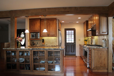 Large elegant u-shaped medium tone wood floor open concept kitchen photo in Denver with an undermount sink, raised-panel cabinets, medium tone wood cabinets, granite countertops, beige backsplash, stone tile backsplash, stainless steel appliances and an island