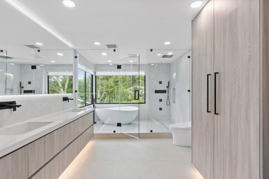 Diseño de cuarto de baño doble moderno con puertas de armario de madera clara, bañera exenta, baldosas y/o azulejos de porcelana, suelo de baldosas de porcelana, encimera de cuarzo compacto, encimeras blancas y hornacina