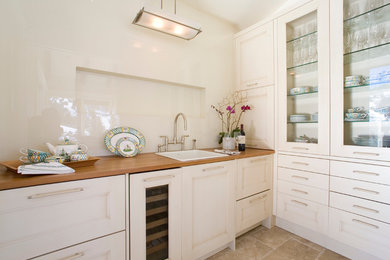 Example of a mid-sized classic single-wall porcelain tile wet bar design in Denver with a drop-in sink, glass-front cabinets, white cabinets and wood countertops