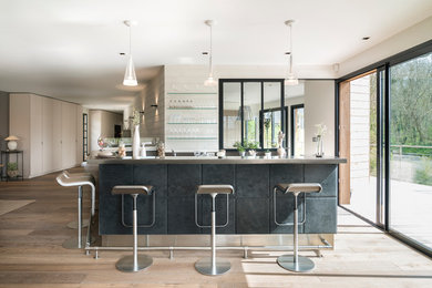 Cette image montre un grand bar de salon design en U avec des tabourets et parquet clair.