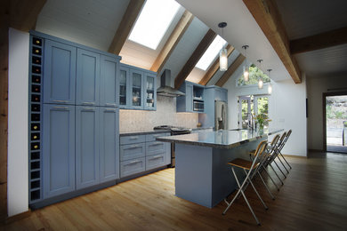 Large trendy single-wall medium tone wood floor and brown floor open concept kitchen photo in Other with an undermount sink, shaker cabinets, blue cabinets, quartz countertops, white backsplash, ceramic backsplash, stainless steel appliances and an island