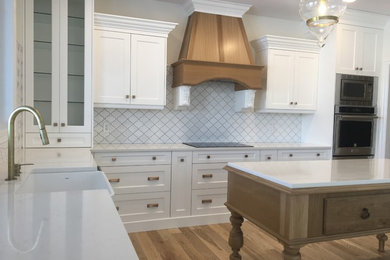 This is an example of an expansive transitional l-shaped kitchen pantry in Other with an undermount sink, recessed-panel cabinets, white cabinets, quartz benchtops, white splashback, ceramic splashback, stainless steel appliances, light hardwood floors, with island and brown floor.
