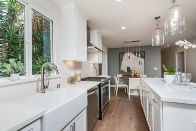 Example of a large transitional single-wall medium tone wood floor open concept kitchen design in San Francisco with a farmhouse sink, white cabinets, stainless steel appliances, an island, shaker cabinets and white backsplash